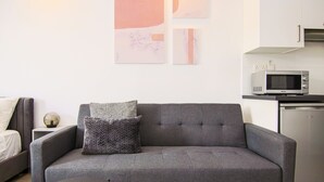 A modern living room with a grey sofa, a small side table with a lamp, and a kitchen area with a microwave and refrigerator. - Phaedrus Living Seaside Flat Athina 115 (Paphos)