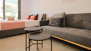 A modern living room with a grey sofa, two round tables, and a bed with a pink blanket. - Phaedrus Living Seaside Flat Athina 115 (Paphos)