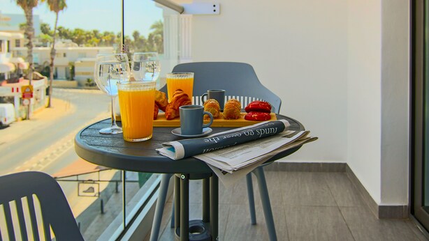 A balcony table with breakfast items including croissants, a cup of coffee, and glasses of orange juice. - Phaedrus Living Seaside Flat Athina 115 (Paphos)