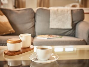 A table with a cup of coffee and two small containers, likely for cream or sugar, in front of a sofa with a blanket. - Pierspeicher Boardinghouse (Kappeln)