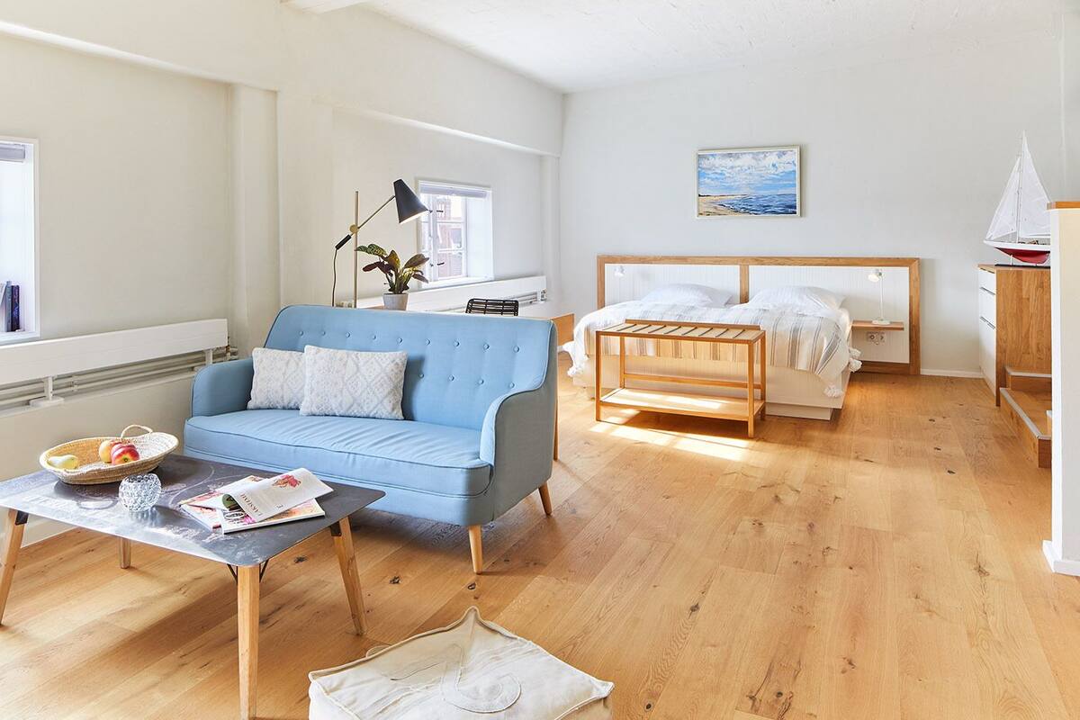 A modern room with a blue sofa, a wooden coffee table, a bed with a wooden frame, and a small sailboat model.