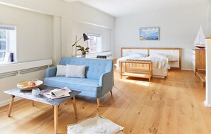 A modern room with a blue sofa, a wooden coffee table, a bed with a wooden frame, and a small sailboat model. - Pierspeicher Boardinghouse (Kappeln)