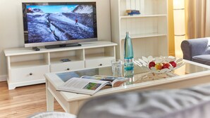 A living room with a flat-screen TV, a glass coffee table with a magazine, a bottle of water, and a fruit bowl. - Pierspeicher Boardinghouse (Kappeln)