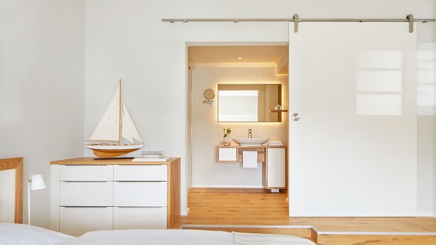 A bedroom with a bed, a dresser, a nightstand, and a sailboat model. - Pierspeicher Boardinghouse (Kappeln)