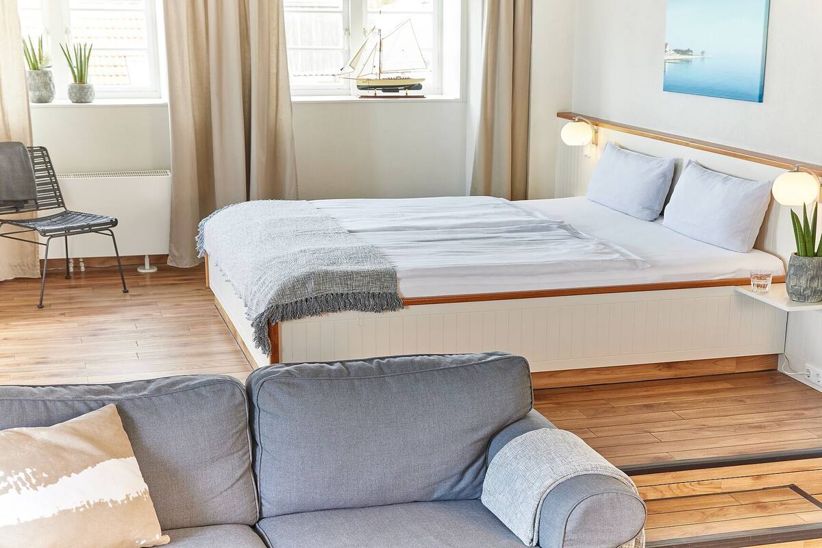 A bedroom with a bed, a chair, a sofa, a small table, and a window with curtains.