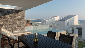 Een moderne buitenruimte met een glazen balustrade met uitzicht op een zwembad en de zee.