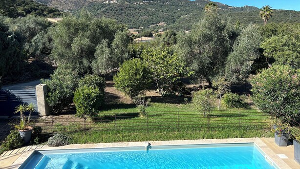 Une piscine offrant une vue sur un paysage montagneux et une zone herbeuse avec des arbres.