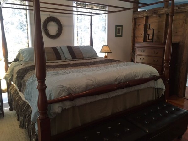 A four-poster bed with a wooden frame and a dark upholstered bench at the foot.