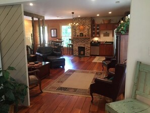 A spacious living room with a fireplace, wooden flooring, and a dining area in the background.