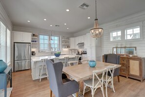 Una cocina amplia con muebles blancos, una isla central y un comedor con mesa y sillas de madera.
