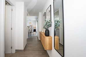 Un couloir avec une console en bois, un grand miroir et des œuvres d’art encadrées.