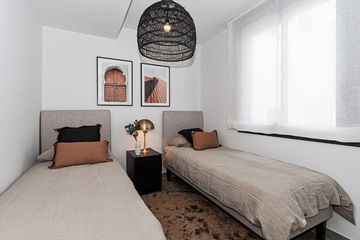 Quarto com duas camas, abajur preto, quadros nas paredes e uma janela grande.