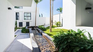 Ein modernes Gebäude mit Wasserspiel, Palmen und einem gepflegten Garten.