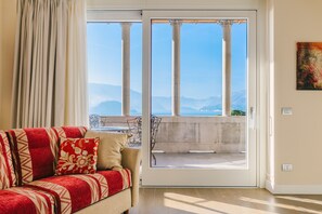 Une pièce avec un canapé, une vue sur un balcon extérieur à travers une porte vitrée et un tableau accroché au mur.