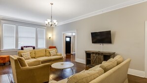 A living room with a beige sofa set, a round coffee table, a flat-screen TV mounted on the wall, and a wooden entertainment center. - Royal Resort (Jackson)