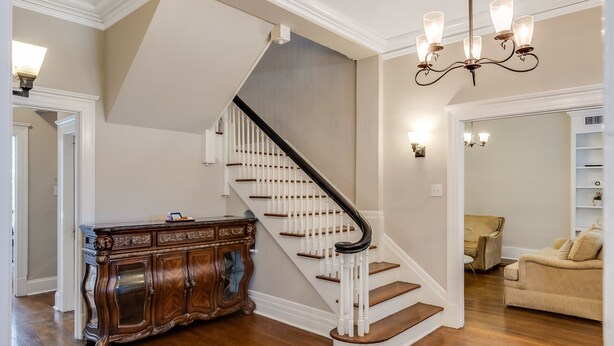 A staircase with white railings and a dark handrail, leading to a landing with a chandelier. - Royal Resort (Jackson)