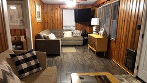 A cozy living room with a sofa, a coffee table, and a television. - Although a country setting, the cottage has all modern conveniences & comforts (Climax)