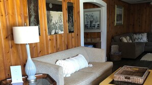 A cozy living room with a beige sofa, a wooden coffee table, and a lamp on a glass table. - Although a country setting, the cottage has all modern conveniences & comforts (Climax)