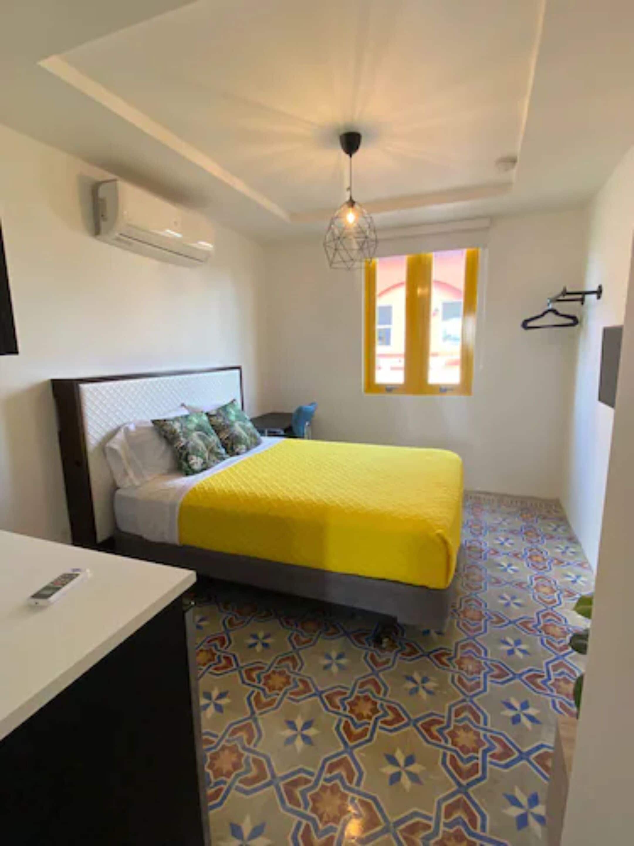 A small, neatly arranged bedroom with a bed, a bedside table, and a hanging light fixture.