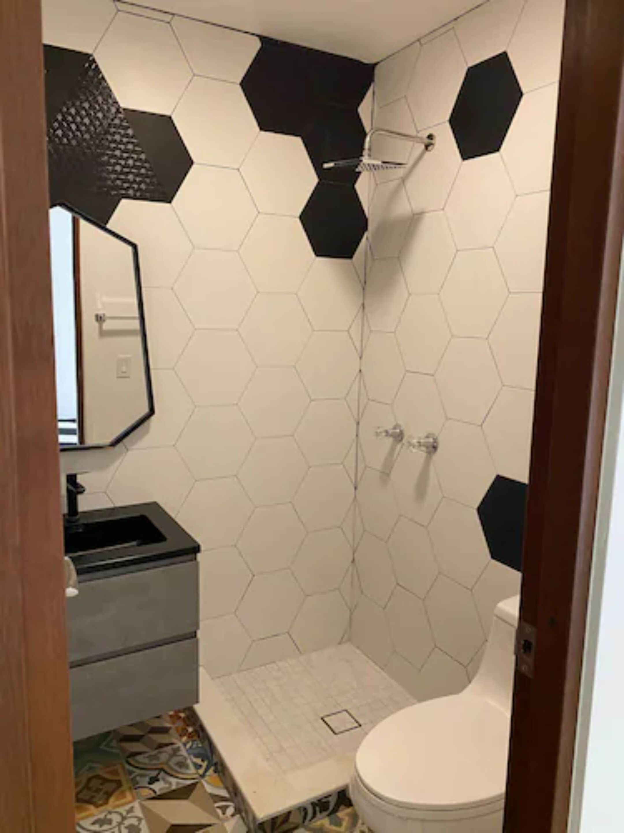 A bathroom with a hexagonal tile pattern, a toilet, a sink, and a shower.