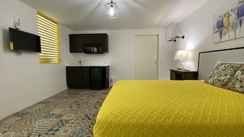 Camera da letto con pavimento a motivi, un letto con copriletto giallo, una TV a schermo piatto, un forno a microonde, un piccolo frigorifero, una lampada e un quadro appeso al muro.