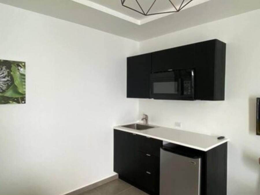 A modern kitchen with black cabinets, a stainless steel refrigerator, and a geometric pendant light.