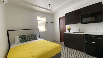 A bedroom with a bed, a window, a kitchen area with a microwave, and a patterned floor.