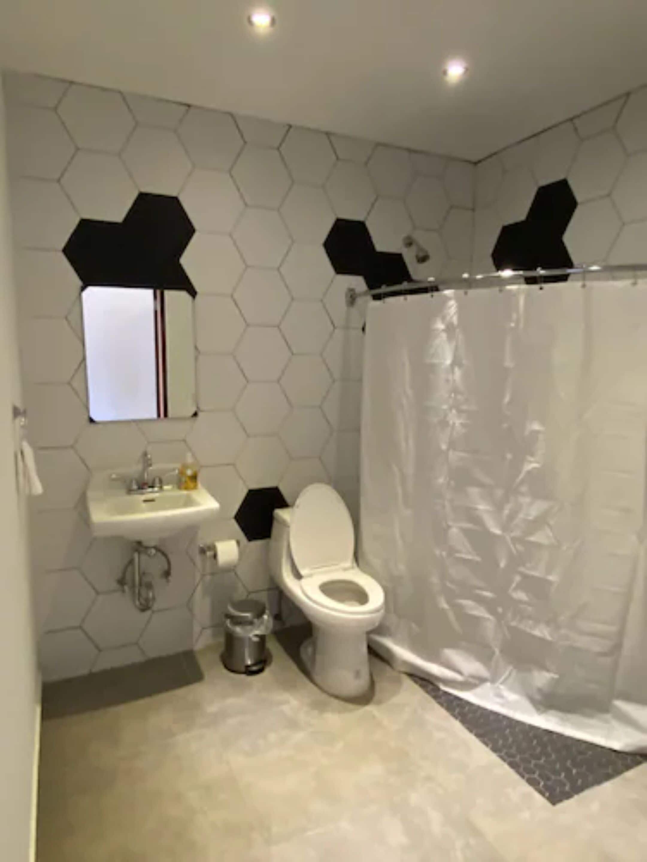 Ein modernes Badezimmer mit einem sechseckigen Fliesenspiegel, einem weißen Waschbecken, einer Toilette und einer Duschvorhang.