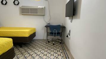 Una habitación con dos camas, un escritorio con silla, un televisor fijado a la pared, aire acondicionado y un suelo con diseño.