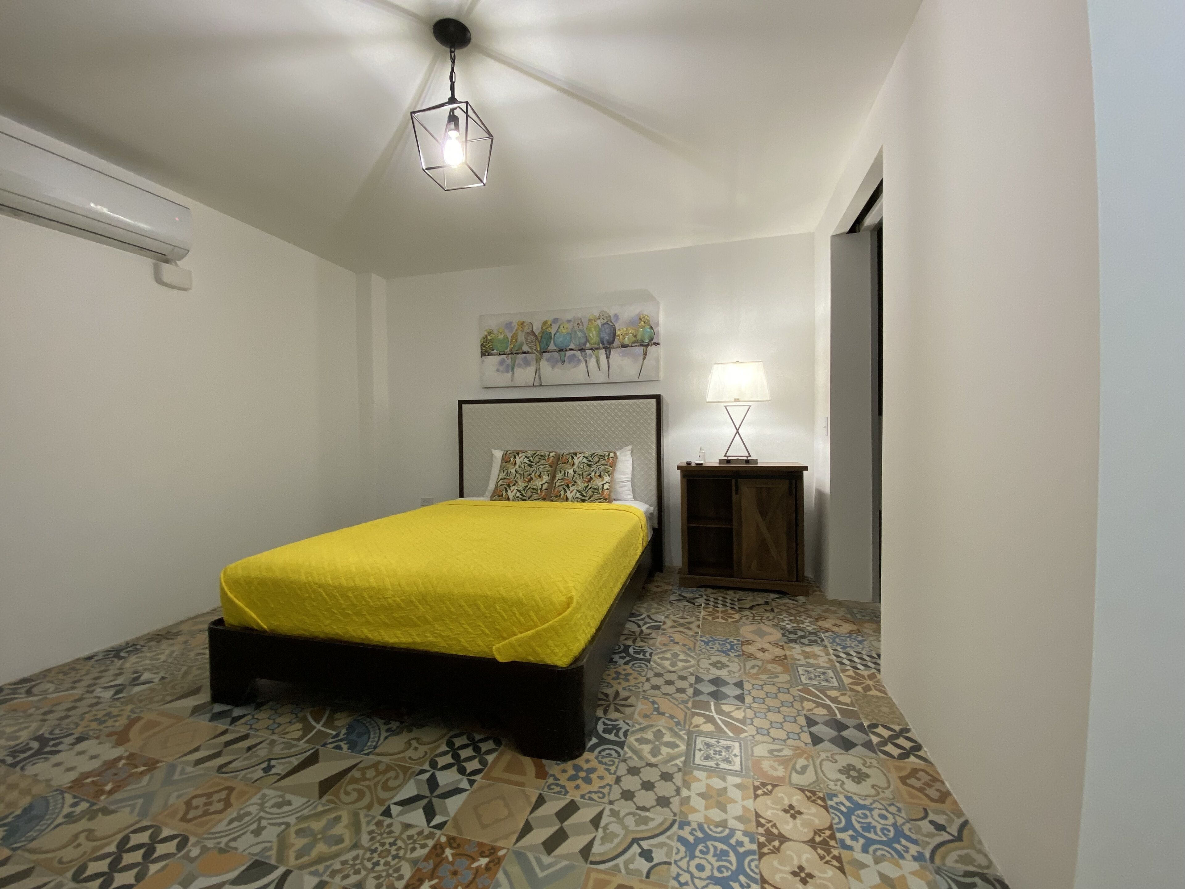 Ein Schlafzimmer mit einem Bett, einem Nachttisch, einer Lampe, einem Deckenventilator und einer Wand mit einem Vogelgemälde.