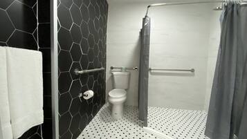 A bathroom with a black hexagonal tile wall, a white toilet, a shower with a grey curtain, and a white towel hanging on a rack.