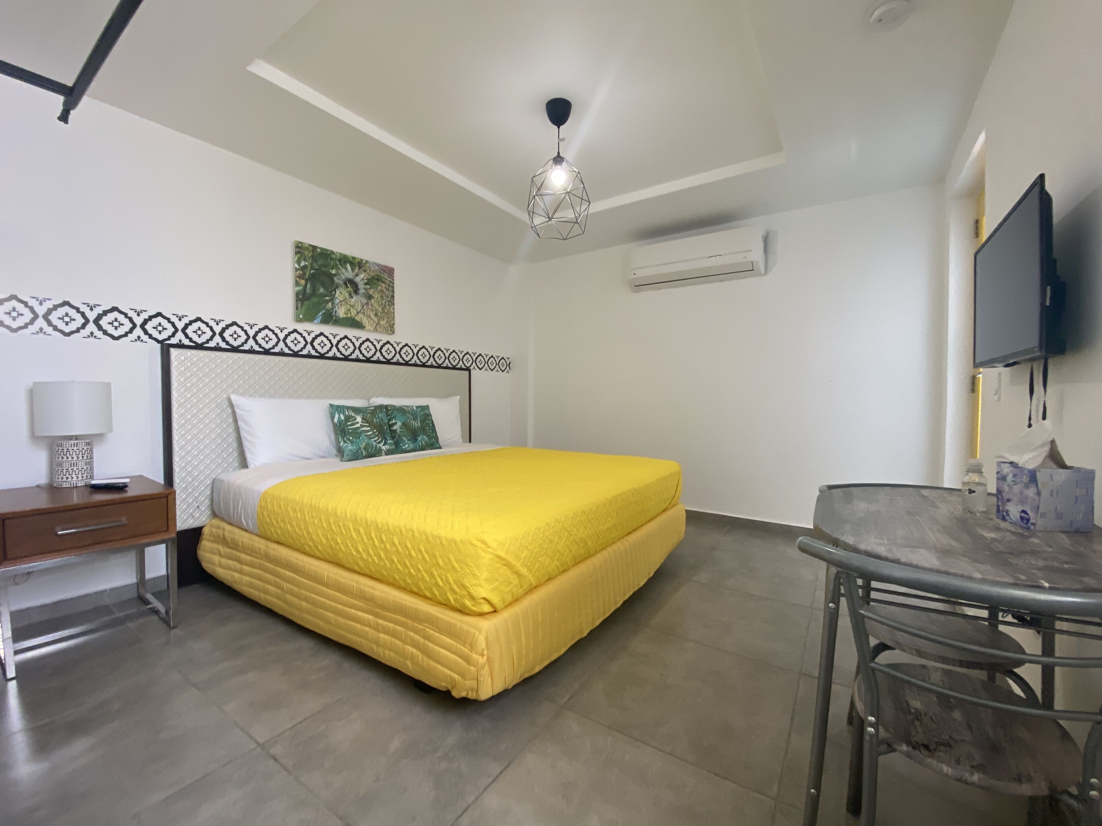 Une chambre d’hôtel équipée d’un lit, d’un bureau, d’une chaise, d’une télévision et d’un luminaire au plafond.