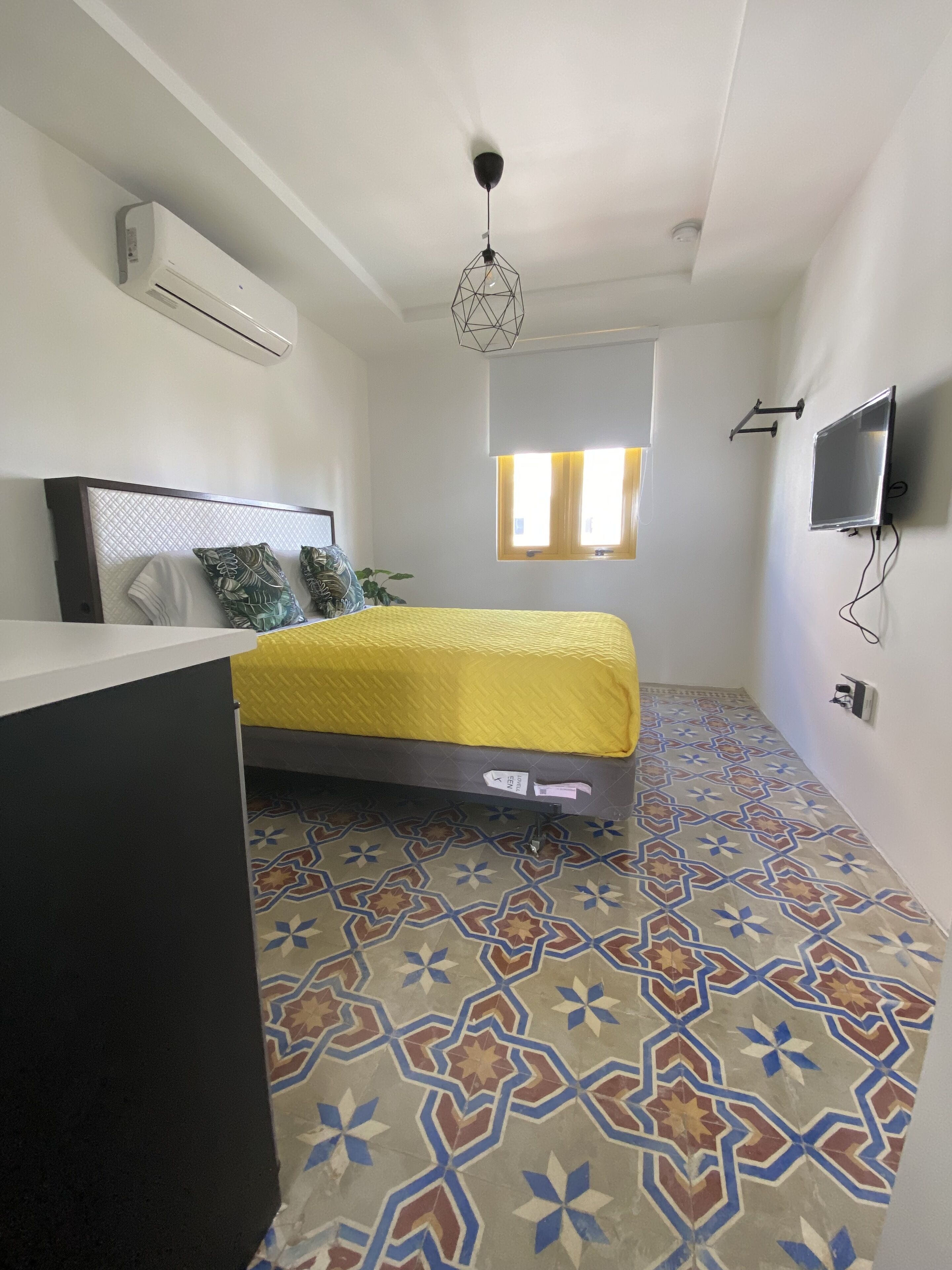 A small, modern bedroom with a bed, a desk, and a TV.