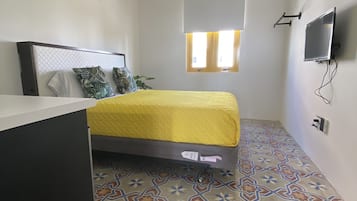 Een kleine, moderne slaapkamer met een bed, bureau en televisie.