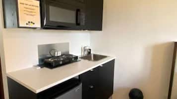 Uma cozinha compacta com armários pretos, micro-ondas, mini-geladeira e piso revestido de azulejos.