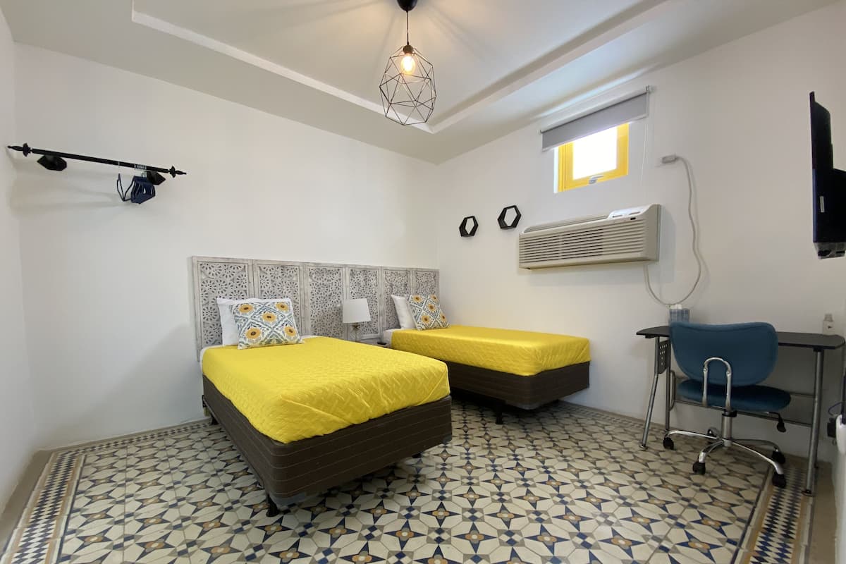 Une chambre avec deux lits, un bureau, une chaise, un téléviseur fixé au mur et un sol à motifs.