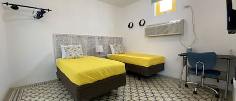 Une chambre avec deux lits, un bureau, une chaise, un téléviseur fixé au mur et un sol à motifs.