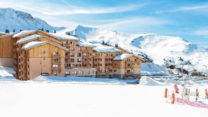 Ein mehrstöckiges Holzhaus mit Balkonen vor einer verschneiten Bergkulisse.