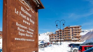 Ein Holzschild mit dem Namen "Odalys Le Front de Neige" und Auflistung der Annehmlichkeiten, darunter ein Restaurant, ein Pool und ein Spa.