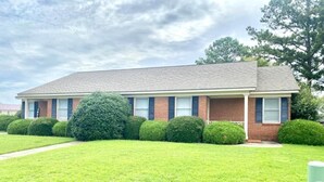 A two-story building with a brick facade, a flat roof, and a front lawn with trimmed bushes.