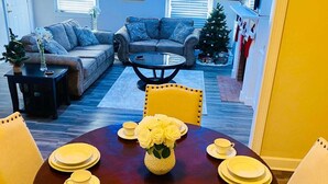 A dining area with a round table set for four, a sofa, and a Christmas tree in the background.
