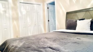 A bedroom with a bed, white doors, and a view of a hallway.