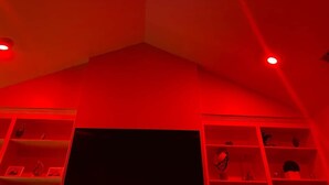 A room with red lighting, a black TV, and shelves with various items.