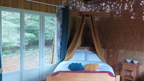 A wooden cabin bedroom with a bed, curtains, and a view of the outdoors.