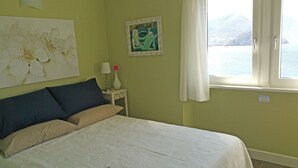 Ein Schlafzimmer mit einem Bett, einem Nachttisch, einer Lampe, einer Vase mit einer Blume und einem Bild an der Wand.