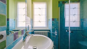 Ein Badezimmer mit einem weißen Waschbecken, zwei Fenstern und einer Duschkabine.