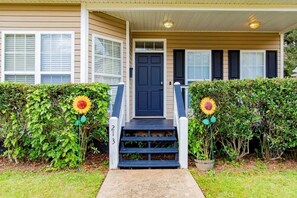 A two-story house with a front door, a number '213' on the steps, and a small garden with sunflowers.