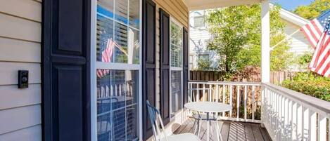 A covered porch with a table and chairs, a white railing, and an American flag.
