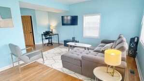 A living room with a sofa, a chair, a coffee table, a TV, and a lamp. - The Bliss Lodge - Large House (Columbus)