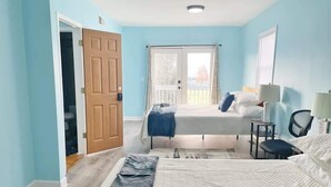 A bedroom with two beds, a wooden door, a balcony, and a view of the outside. - The Bliss Lodge - Large House (Columbus)